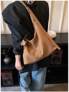 Gros plan d'un sac hobo en daim marron avec surpiqûres blanches porté à l'épaule