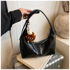 Detail of black woven hobo tote bag with silver zipper and fuzzy charm on casual background