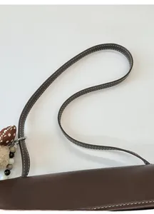 Detail of dark brown leather tote with white stitching and cute heart bead charm