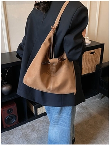Sac hobo en daim marron avec surpiqûres blanches porté à l'épaule par un mannequin