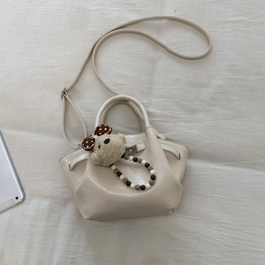 Detail view of cream crossbody bucket bag with cute plush bear and beaded chain charm