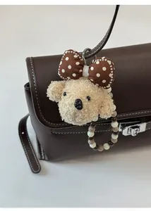 Detail of cute beige plush bear pendant with polka dot bow and beaded chain on leather bag
