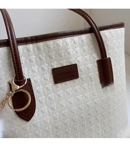 Close-up of star embossed white tote bag with deep brown leather trim and golden logo