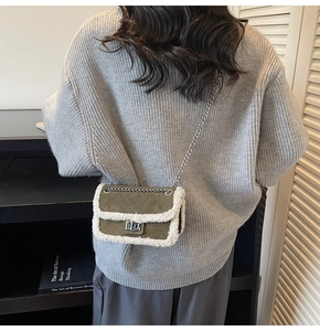 Green suede quilted handbag with white faux fur trim and silver chain on grey sweater