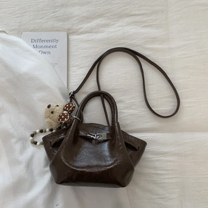 Detail of dark coffee oily leather bag with silver lock and plush bear charm
