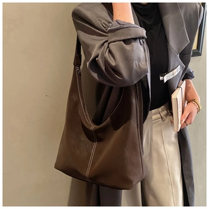 Détail macro du sac hobo en daim marron foncé avec surpiqûres blanches sur la bandoulière