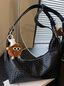 Black woven hobo shoulder bag with a designer plush monster pendant in a minimalist setting