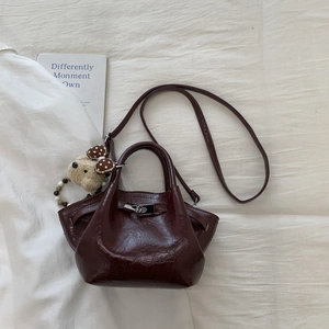 Detail view of burgundy pleated patent leather bucket bag with silver lock and plush bear charm