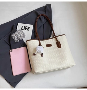 Flat lay of cream woven tote bag with brown straps, tablet, book and chic office accessories