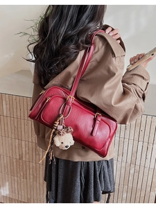 Detail of red leather bowling bag with side pockets and fluffy bear charm on model