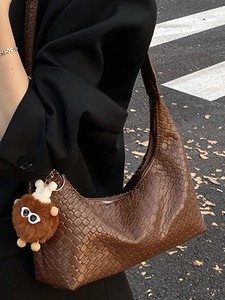 Brown woven crescent tote bag with cute plush pendant styled with a black blazer