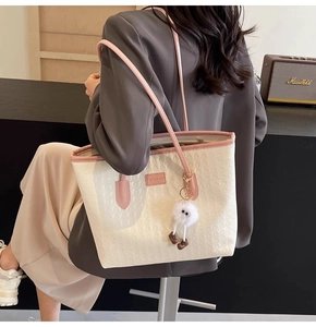 Detail of cream woven tote bag with pink trim and cute plush charm on a shoulder strap
