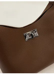 Detail of lychee pattern leather and silver metal twist lock on a brown shoulder bag