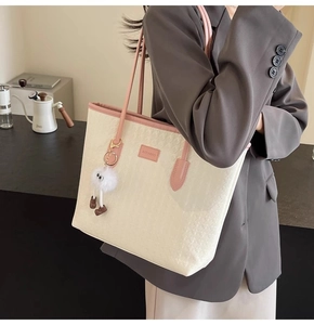 Detail of off-white tote bag with pink trim and cute plush doll pendant on a shoulder strap
