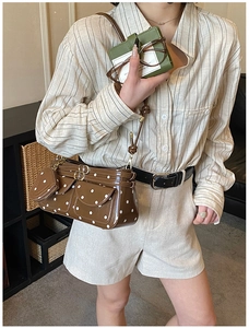 Close-up of a brown polka dot crossbody bag with a round charm and shiny finish