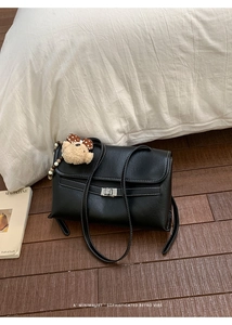 Detail view of black PU leather shoulder bag with white stitching and plush bear charm