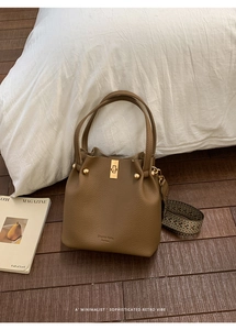 Detail of brown lychee leather bucket bag with wide ethnic woven strap and gold hardware