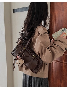Close-up of retro brown Boston bag with plush puppy charm and ribbon on model's shoulder