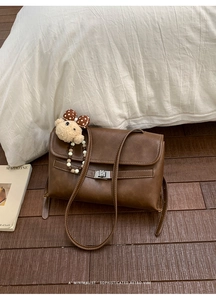 Detail view of a vintage brown crossbody bag featuring a metal lock and a cute bear charm