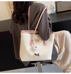 Detail of cream and pink tote bag with woven texture and a plush charm on model
