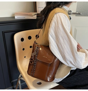 Detailed close-up of brown oiled leather bucket bag with gold logo and woven rope charm