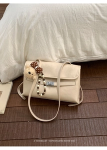 Close-up of retro cream leather shoulder bag with silver buckle and plush bear charm