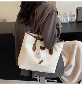 Detail of woven tote bag with brown leather handles and a plush doll charm on the side