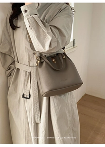 Detailed view of a taupe leather bucket bag with jacquard strap worn with a trench coat
