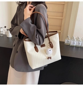 Detail of cream woven tote bag with dark brown straps and white plush pendant