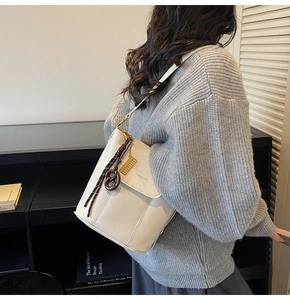 Close-up of cream bucket bag with woven rope charm and gold logo plate detail