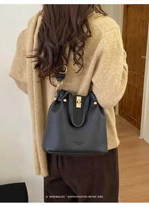 Detail of black lychee grain leather bucket bag with gold twist lock on model's shoulder