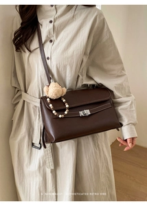 Detail of dark brown leather crossbody bag featuring silver hardware and a plush bear charm