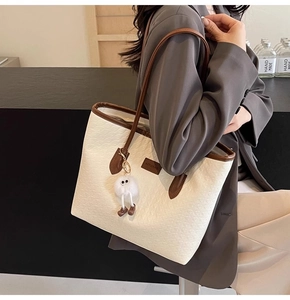 Detail of white textured tote bag with brown trim and plush ball pendant on shoulder