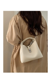 Detailed macro view of the cream lychee-grain leather texture and silver buckle on bucket bag