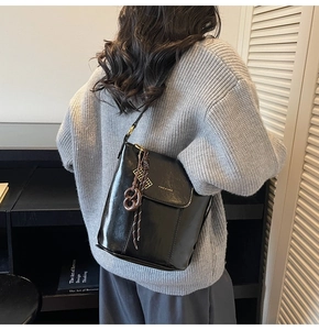 Chic black shiny leather bucket bag with logo and knot charm shown on a casual grey outfit