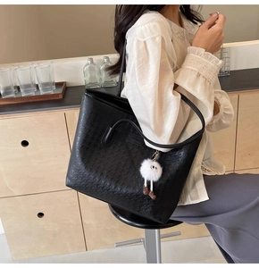 Detail of black tote bag with geometric texture, white plush charm, and leather handle