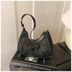 Close-up of black lace underarm bag with 3D butterfly embroidery on a book