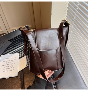 Close-up of a retro dark brown bucket bag with gold logo and tassel detail on a desk