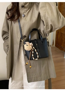Detail of black pebbled leather bucket bag featuring cute bear charm and colorful beads