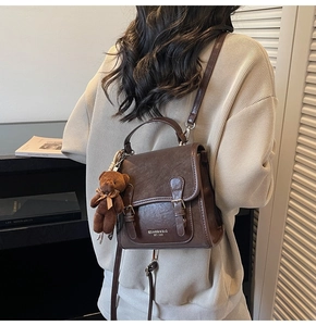 Detalle de una mochila vintage de cuero marrón con colgante de osito y hebillas metálicas