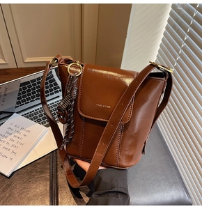 Detail of a brown leather bucket bag featuring a ribbon tassel and branded logo plate