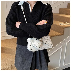 Polka dot crossbody bag with heart-shaped charm shown on a model in a casual indoor setting