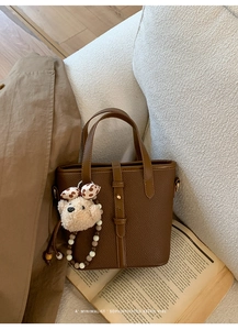 Detail of brown lychee grain leather bucket bag with cute plush bear and beaded charms