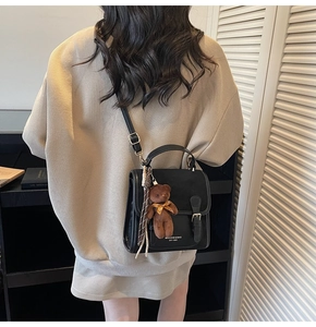 Detalle de bolso de cuero negro con hebilla metálica y colgante de oso de peluche