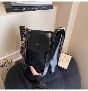 Close-up of black glossy leather bucket bag with golden logo and vintage abacus charm