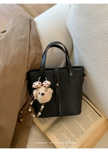 Close-up of black lychee leather tote bag featuring a cute plush bear charm with beads