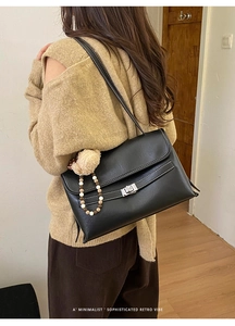 Detail of black leather shoulder bag with white stitching and silver twist-lock on a model