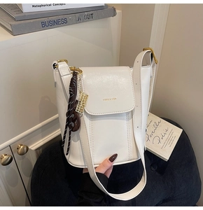 Detail shot of white leather bucket bag featuring gold logo and woven pendant