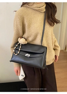 Close-up of black crossbody bag featuring contrast stitching and a cute bear charm