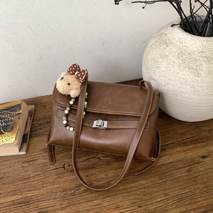 Detail of vintage brown leather bag with silver twist lock and bear charm on wood table